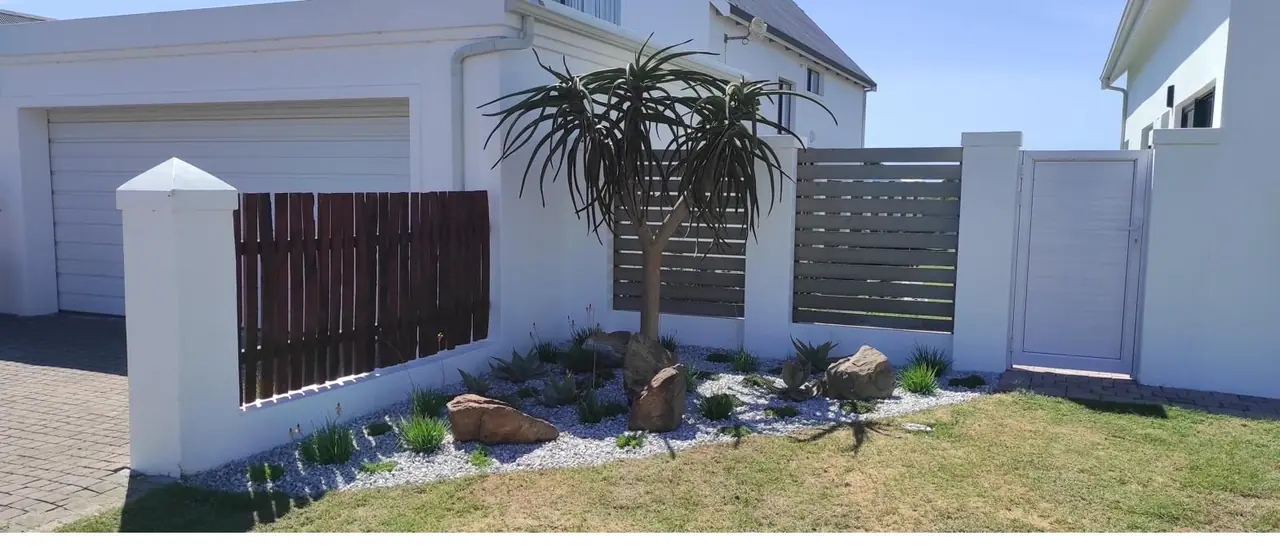 Finished coastal boundary garden with a tree aloe, boulders and white decorative stone in St Francis Bay