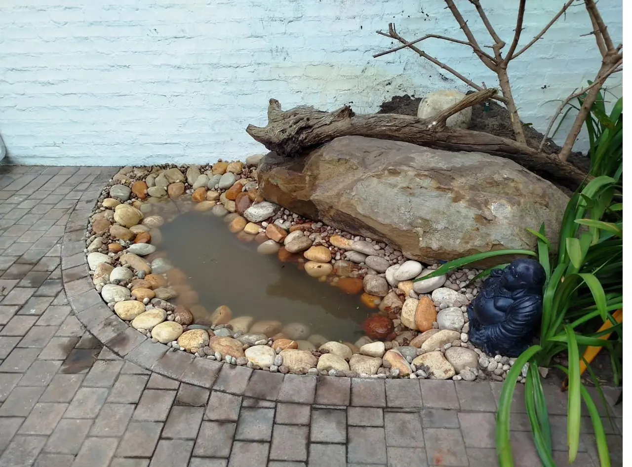 Natural stone water feature edged with rounded river stones, a boulder and driftwood